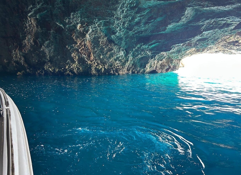 A boat in a clear blue sea with a rocky cave entrance. 3