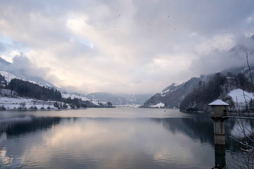 A calm lake surrounded by snow-covered mountains and a small tower structure. 3