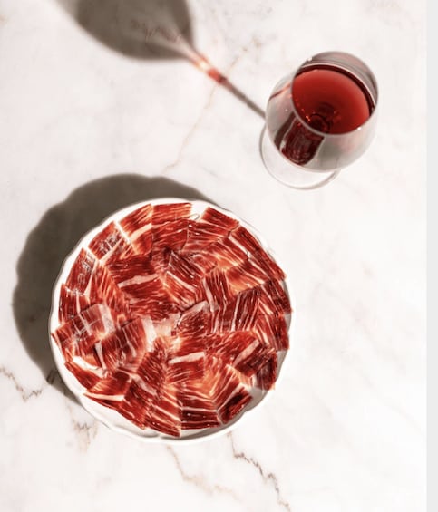 A plate of thinly sliced meat, possibly prosciutto, on a marble surface with a glass of red wine. 5