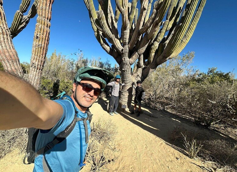A person taking a selfie with a large cactus and a clear blue sky in the background. 3