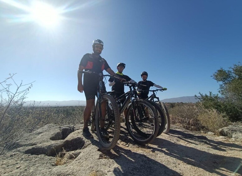 Three people standing on rocky terrain with bicycles, under a clear sky. 5