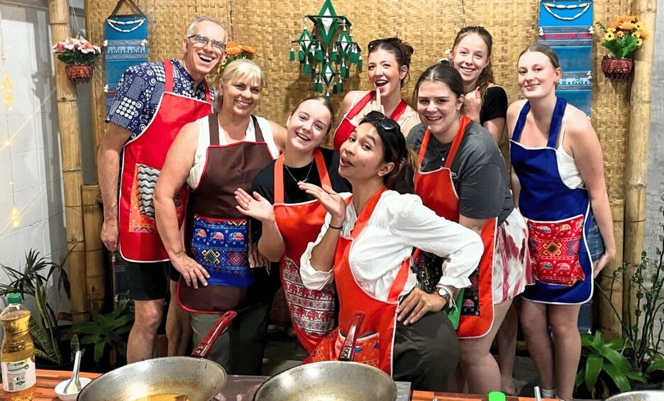 A group of people in aprons posing in a kitchen with bamboo walls and decorative elements. 4