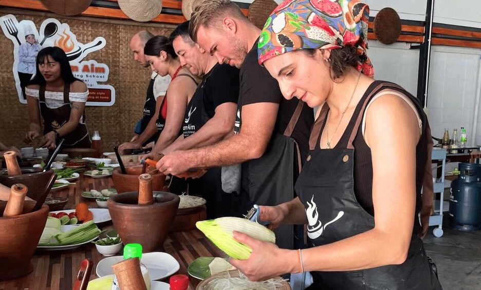 People preparing food at a cooking station with wooden utensils and fresh vegetables. 1