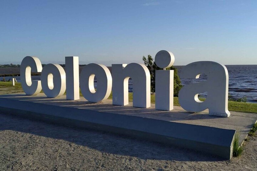 Large white letters spelling "Colonia" on a concrete platform by the sea. 1