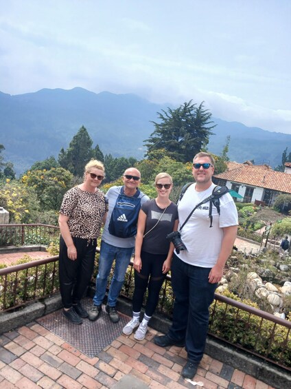Four people standing on a balcony with a mountainous landscape in the background. 3