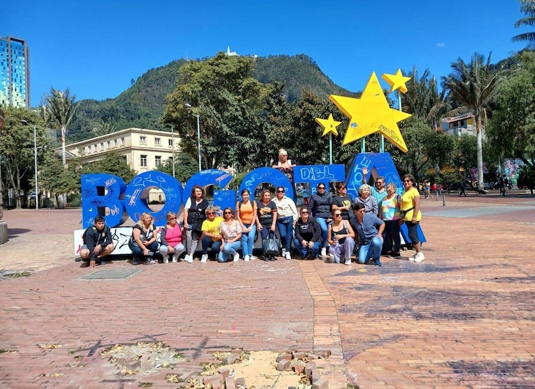 A group of people posing in front of a large blue sign with the word "ROGOTIA" and two yellow stars. 1