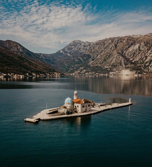 A small island with a church and a bell tower, surrounded by calm water and mountains. 2