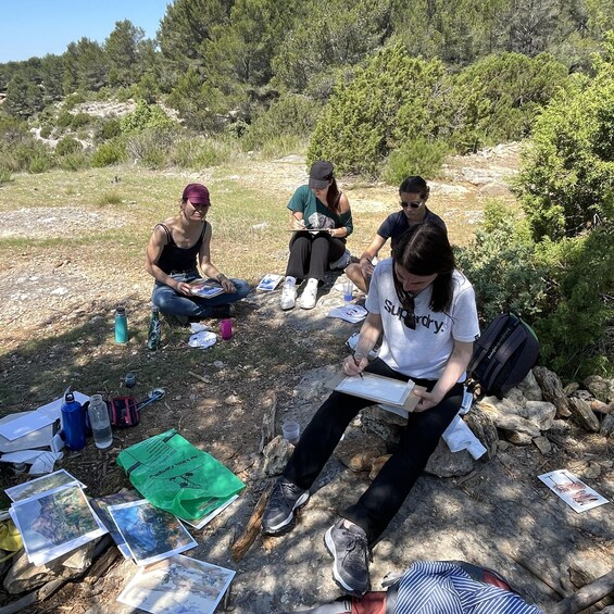 Three people sitting on rocks outdoors with art supplies and papers. 4