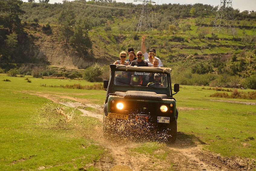 A group of people on a safari tour in a vehicle driving through a grassy field. 4