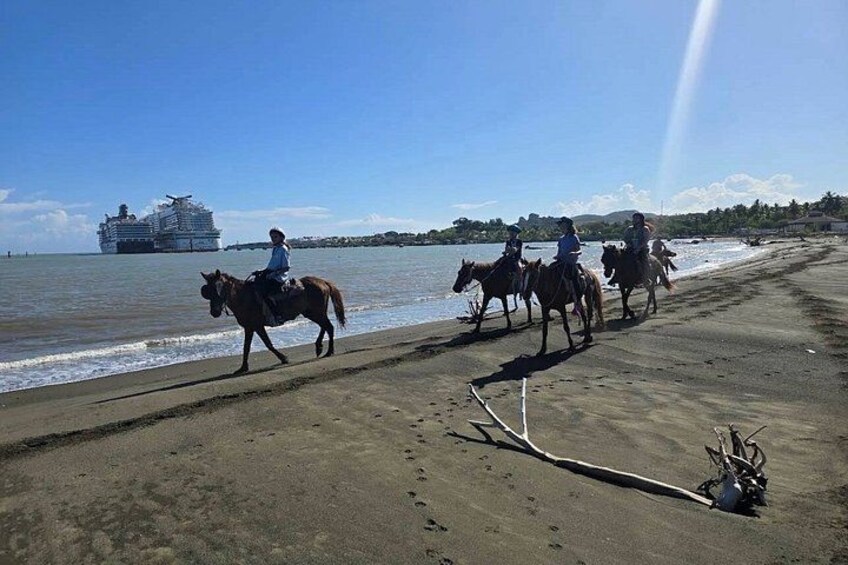 A beach with people riding horses, a cruise ship in the background, and a clear sky. 5