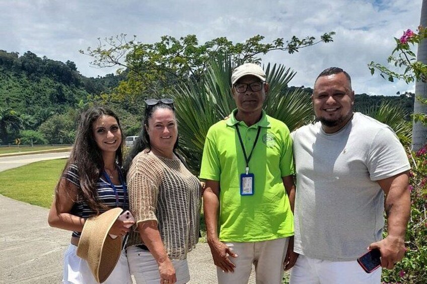 Four people standing outdoors with greenery and hills in the background. 3