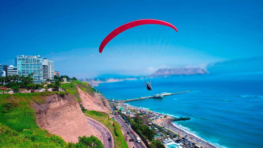 Un parapentista vuela sobre una zona costera con edificios y una playa. 1