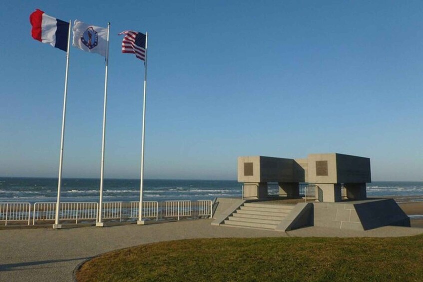 A coastal walkway with flags, a modern structure, and the ocean in the background. 1