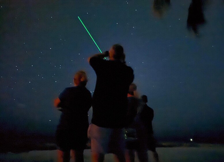 A group of people observing the night sky, with a visible green laser beam. 2