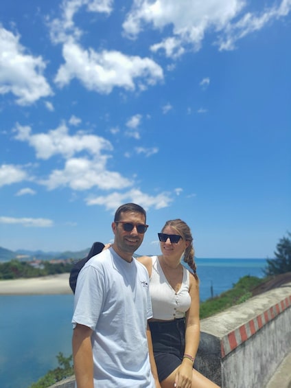 Two people standing by a waterfront with a clear sky and distant mountains. 3