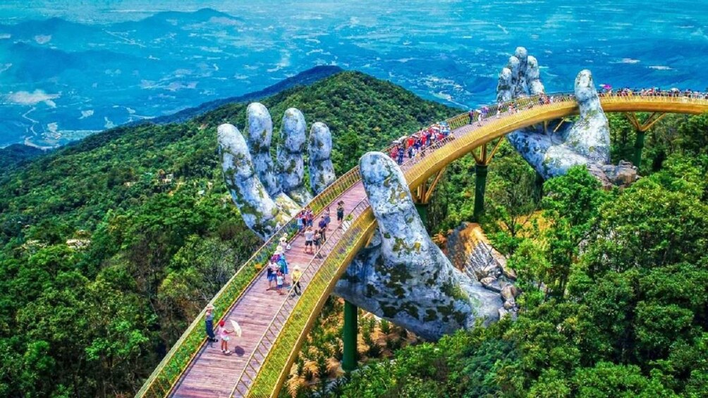 A bridge with large hand-shaped supports over a forested area. 1