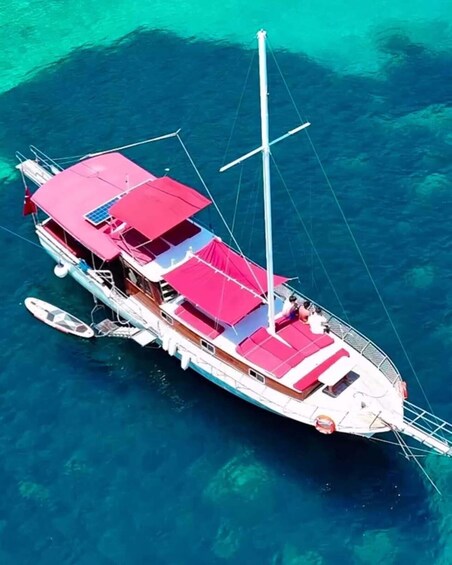 A large boat with multiple decks and a tall mast, anchored in clear blue water. 3