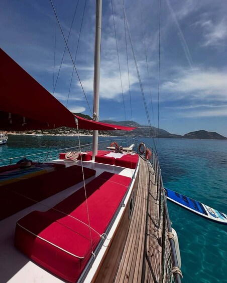 A sailboat with red cushions on the deck, anchored near a coastline with clear blue water and distant hills. 4