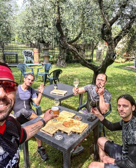 Four people sitting at an outdoor table with food and drinks, surrounded by greenery and trees. 1
