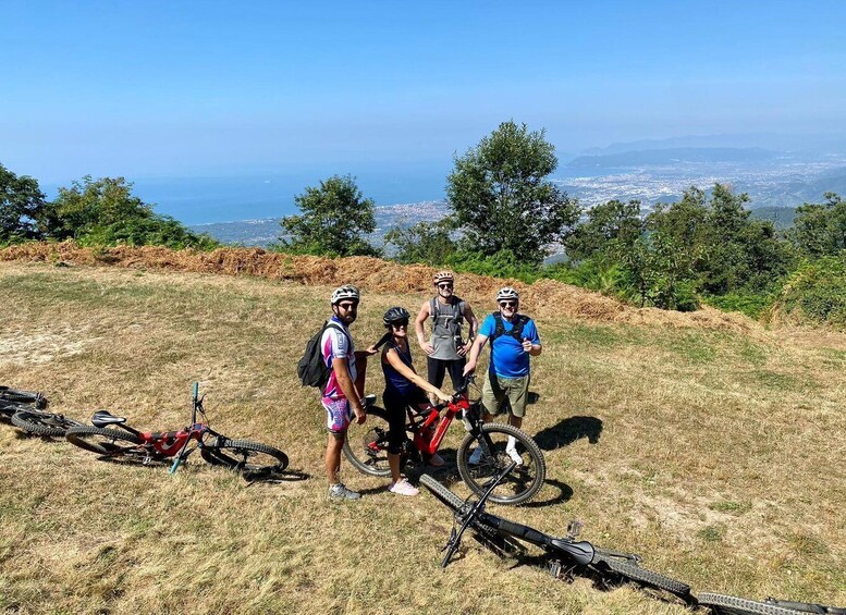 Four people standing on a grassy hill with bicycles, overlooking a cityscape and the ocean. 2