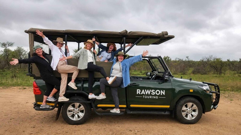 En grupp människor sitter i ett grönt safari-fordon med texten ”RAWSON TOURING” på sidan. 1