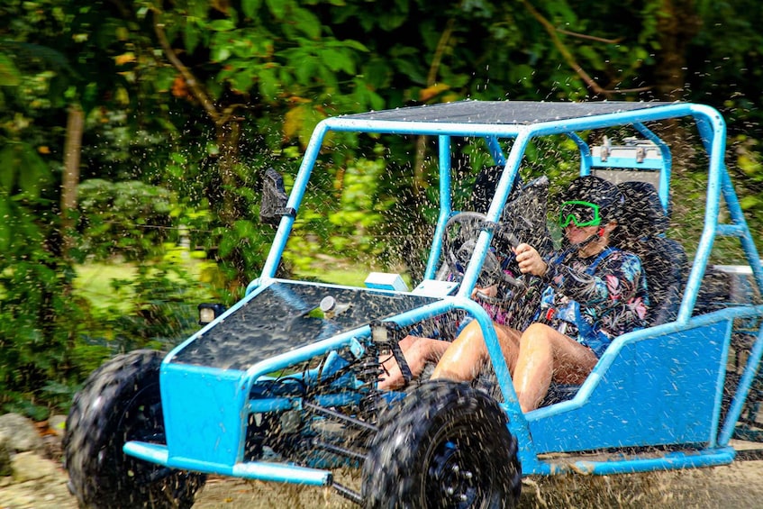 A blue off-road vehicle in motion, surrounded by greenery. 1