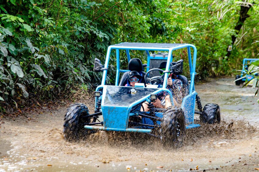 A blue off-road vehicle driving through a muddy path surrounded by dense greenery. 2