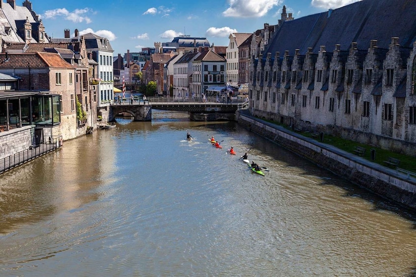 A river with kayakers in a row, a bridge, and historic buildings along the banks. 2