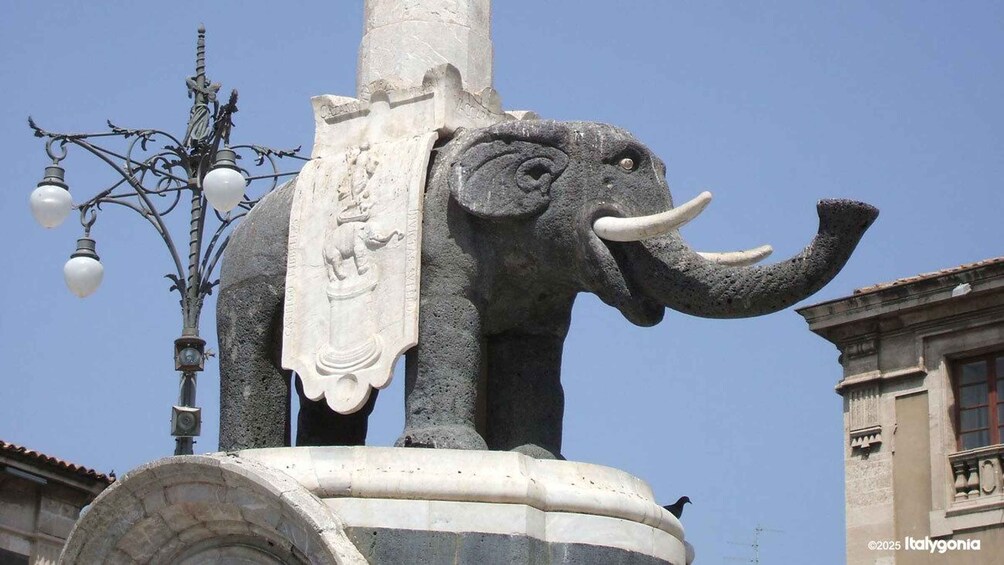 A stone elephant statue with a draped cloth, a street lamp, and a building in the background. 3