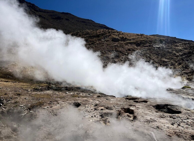 A geothermal area with steam rising from the ground, surrounded by rocky terrain and a clear sky. 5