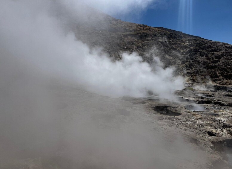 A volcanic landscape with steam rising from the ground, indicating geothermal activity. 2