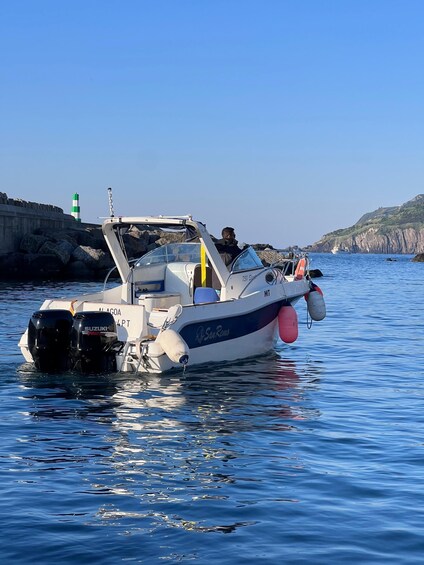 A boat named 'San Remo' anchored near a rocky coastline with a lighthouse in the background. 1