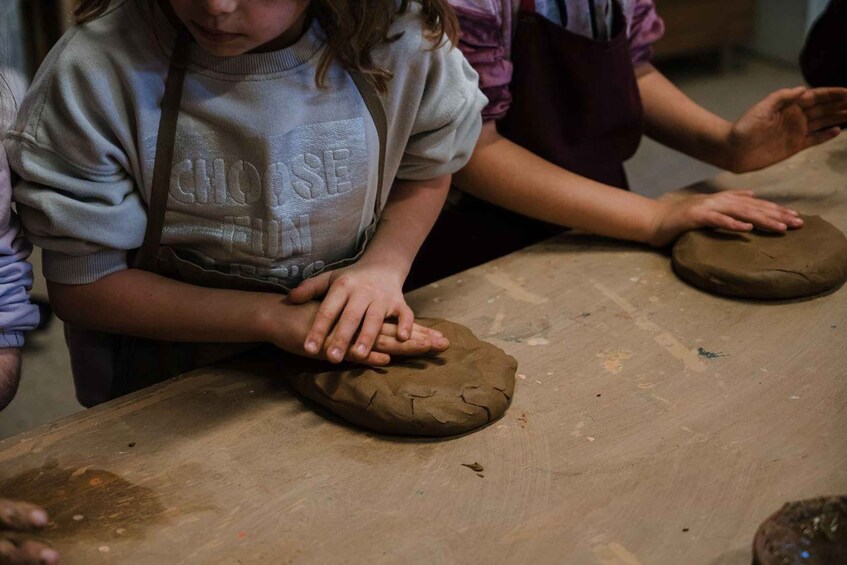 A person shaping a clay object on a wooden table. 1
