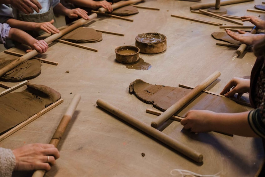 A group of people engaged in pottery making, using rolling pins and clay on a table. 4