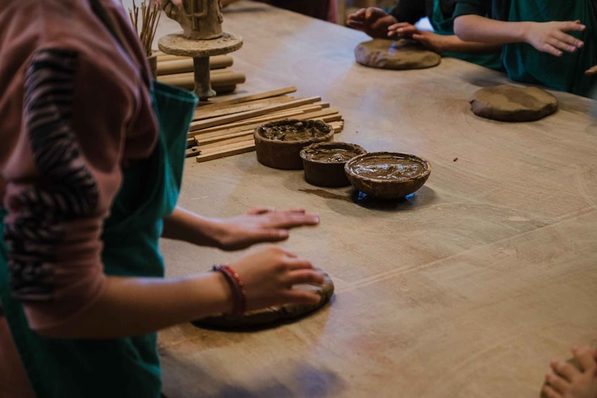 A group of people engaged in pottery making, with clay pots and tools on a table. 2