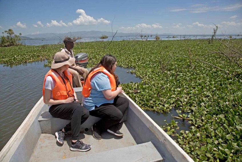 Three people in a boat surrounded by water with floating vegetation. 3