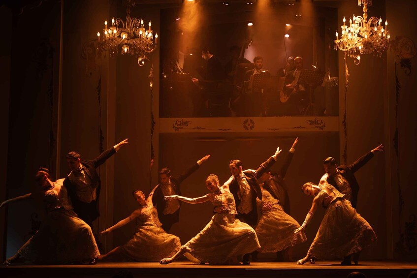 A stage with dancers in period costumes, a chandelier, and a mirror reflecting the scene. 5