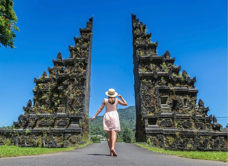 A woman walking towards a temple entrance with intricate carvings and lush greenery. 1