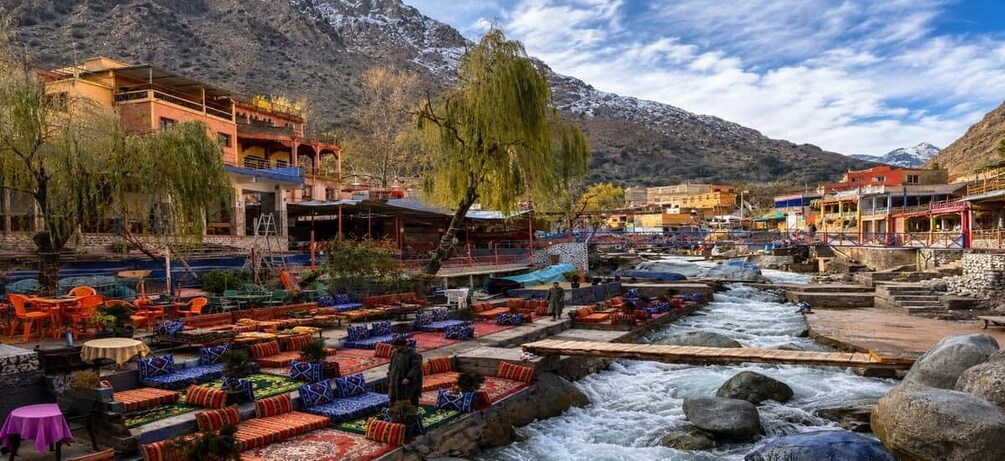 A riverside café with outdoor seating, a mountain backdrop, and a flowing river. 2