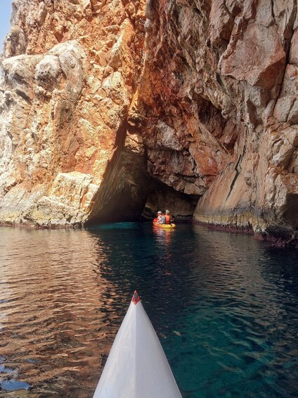 A rocky cliff with a cave entrance, clear blue water, and a white boat with a red bow. 5