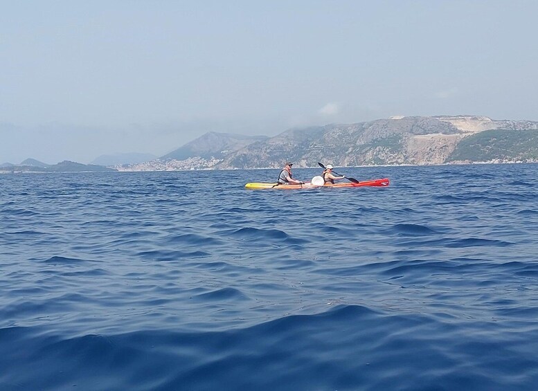 Two people kayaking on a calm sea with a mountainous coastline in the background. 5