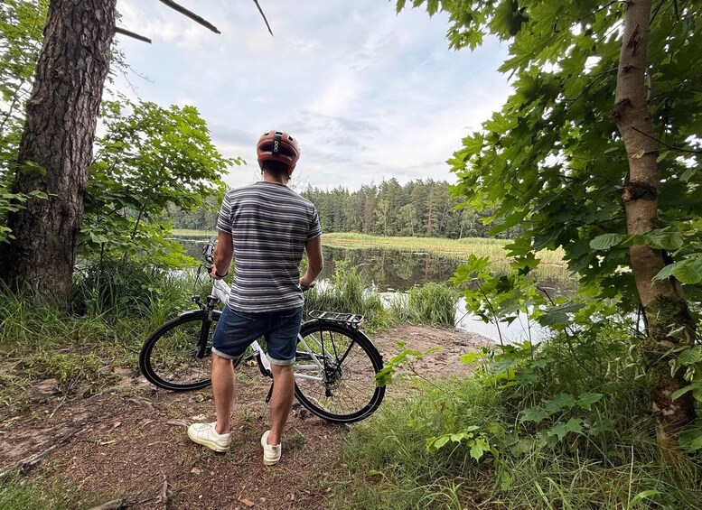 A person standing by a lake with a bicycle, surrounded by trees and greenery. 2