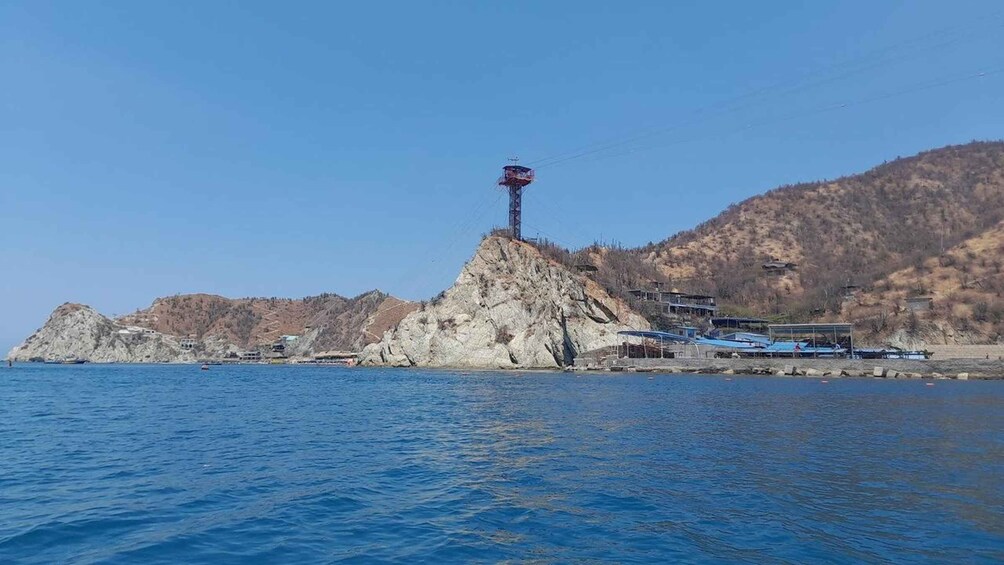 A rocky island with a flagpole in the center, surrounded by calm blue water and a hilly landscape in the background. 4