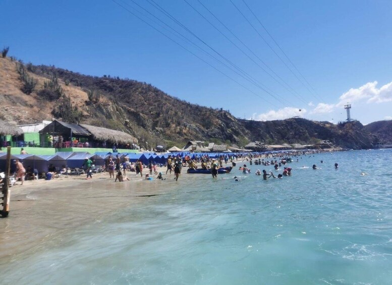 A crowded beach with people swimming and sunbathing, tents, and a hilly landscape in the background. 5