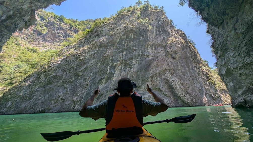 A person kayaking in a river with a rocky cliff in the background. 1