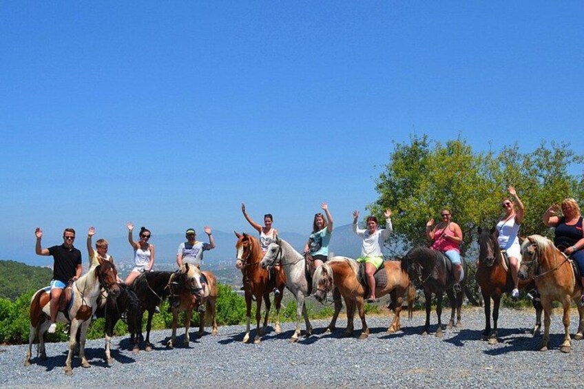 Un grupo de personas montando a caballo sobre un sendero de grava, con un cielo despejado y vegetación al fondo. 3