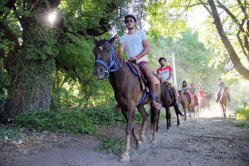 Un grupo de personas montando a caballo por un sendero de tierra rodeado de árboles. 2