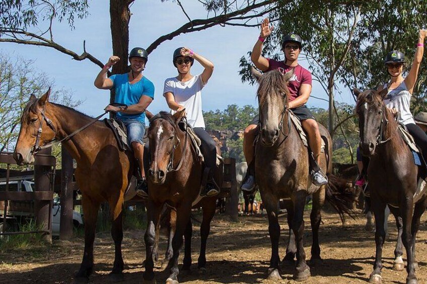 Personas montando caballos por un sendero de tierra, con árboles y una cerca al fondo. 1