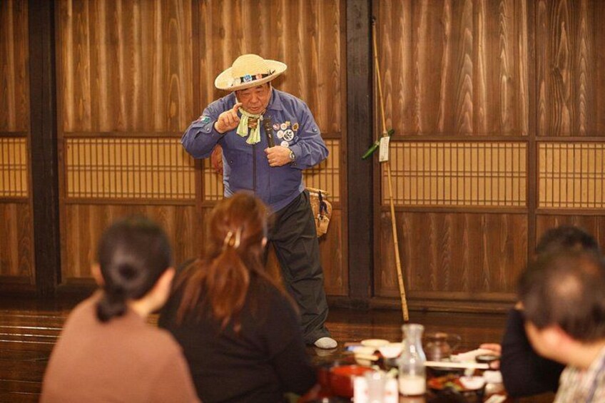 A person in a blue shirt and straw hat performing with a microphone in front of an audience. 2