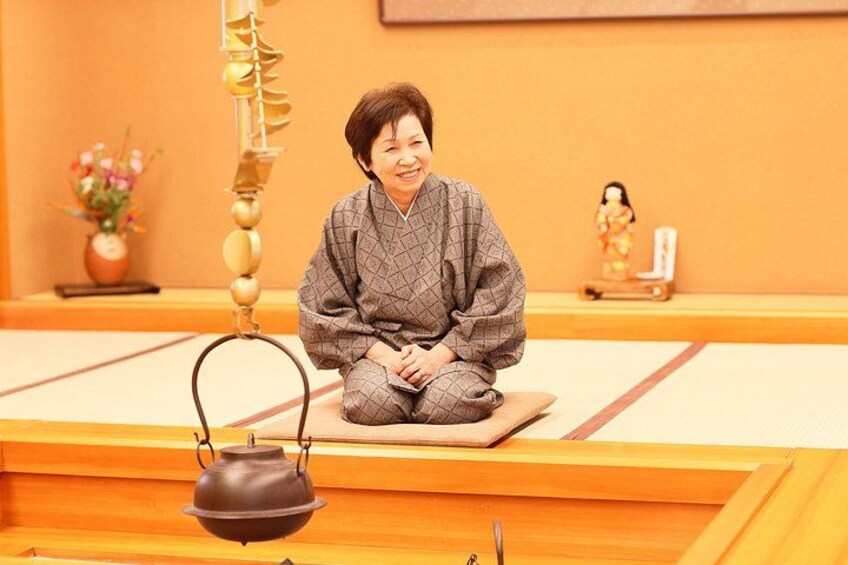 A person sitting on tatami mats in a traditional Japanese room with a tea kettle in the foreground. 3